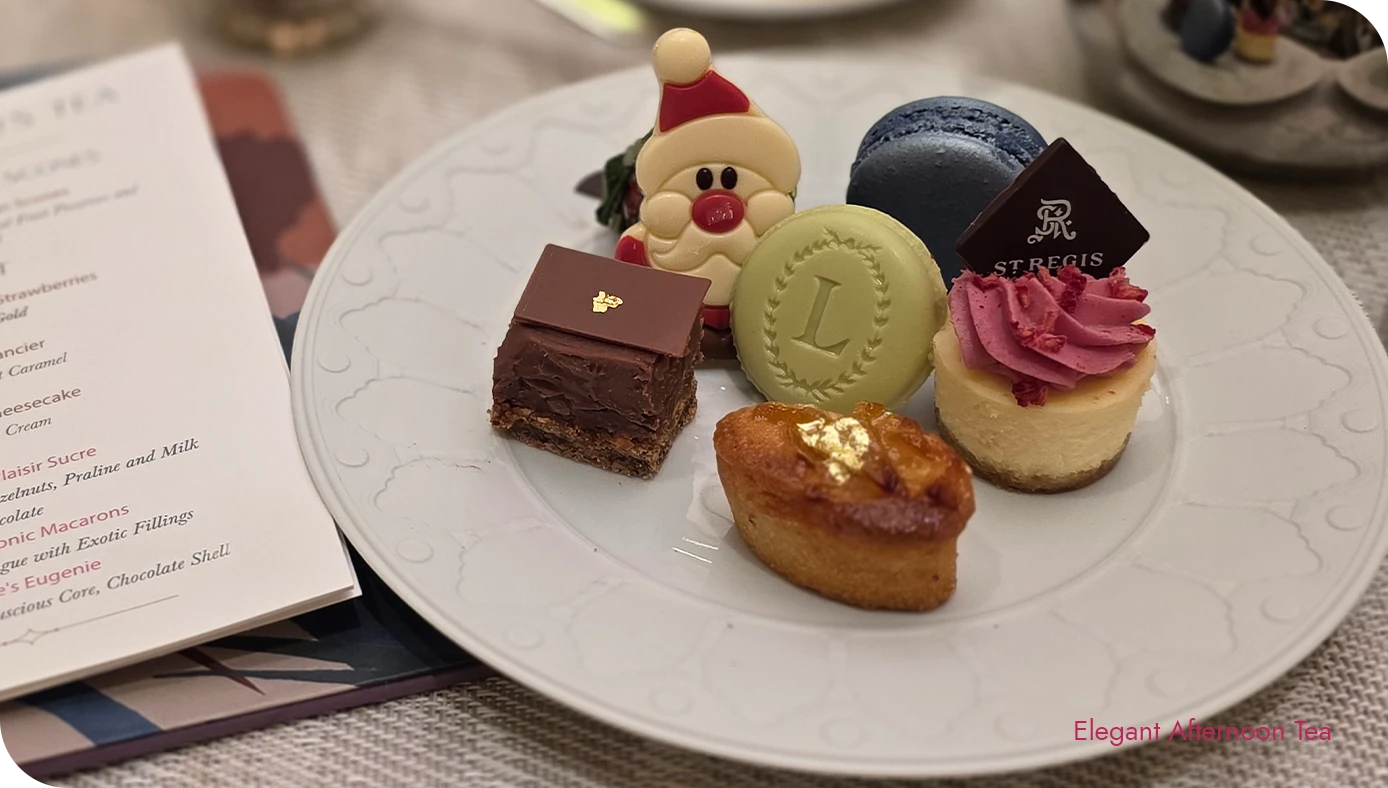 Holiday afternoon tea desserts arranged on a plate beside the Lady Astor’s Tea menu and a cup of tea at the St. Regis New York