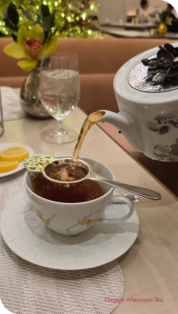 Tea being poured through a silver strainer into a teacup during St. Regis afternoon tea