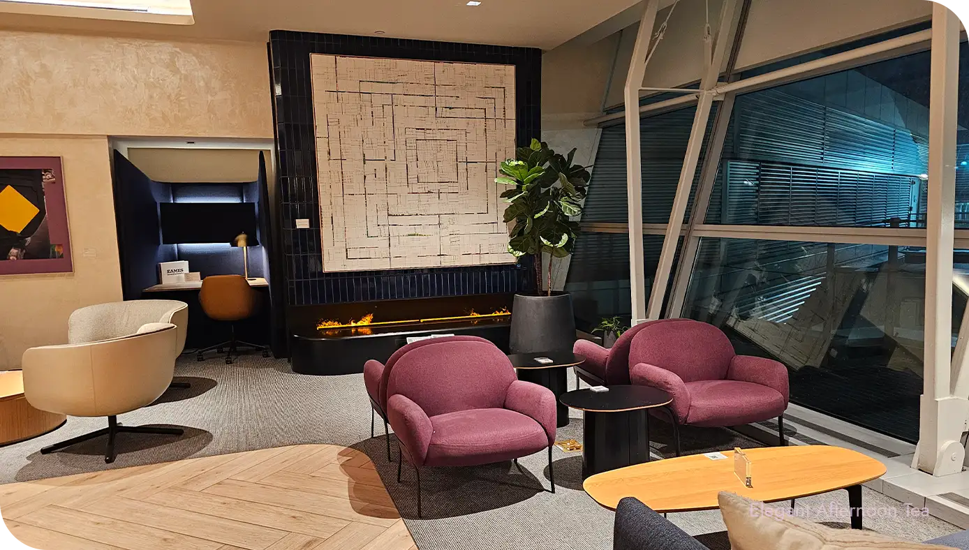 Seating nook with mauve lounge chairs near windows and a fireplace in the background.